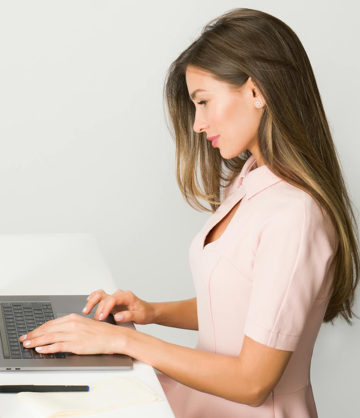 Photo by Moose Photos A woman in a pink dress working on a laptop at a modern, minimalist desk.